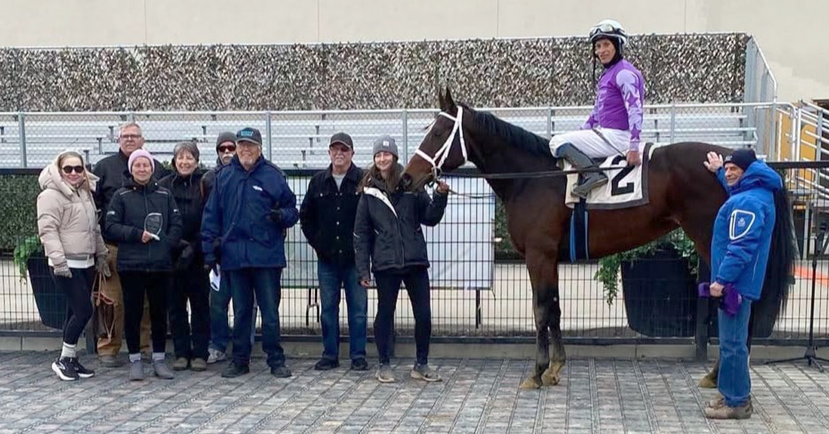 A group of people standing with a horse and jockey in the winners circle.
